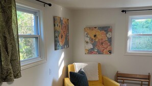 A room with a yellow armchair, a bed with a pink blanket, two windows with curtains, and floral artwork on the walls. - Spacious Chester Home with Spectacular Ocean Views! (Chester)