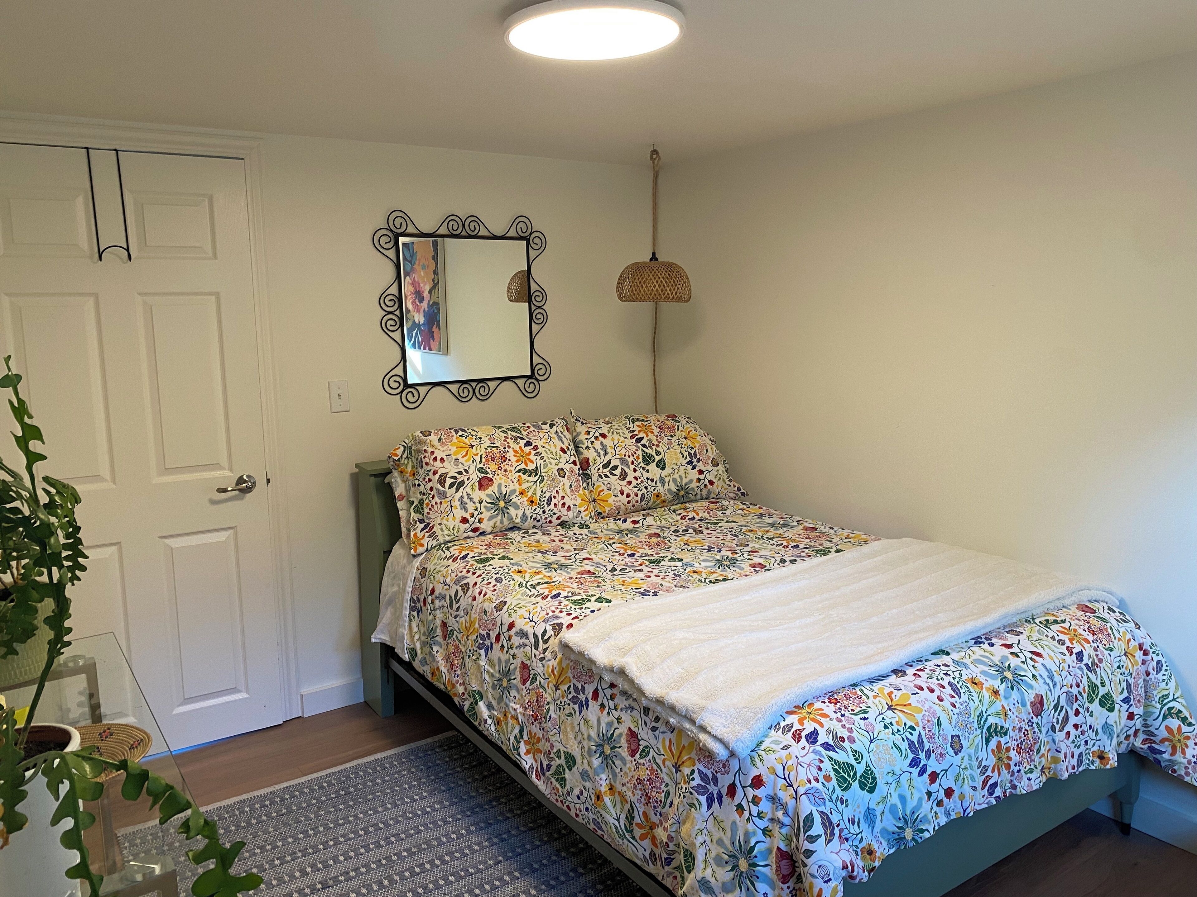 Un dormitorio con colcha estampada, lámpara colgante y espejo en la pared.