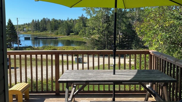 A wooden deck with a picnic table and a yellow umbrella, overlooking a lake and forest. - Spacious Chester Home with Spectacular Ocean Views! (Chester)