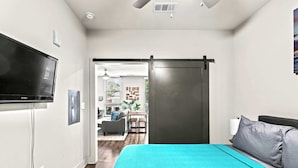 Quarto de hotel moderno com uma cama grande, televisão de tela plana na parede e porta deslizante para uma área de jantar.