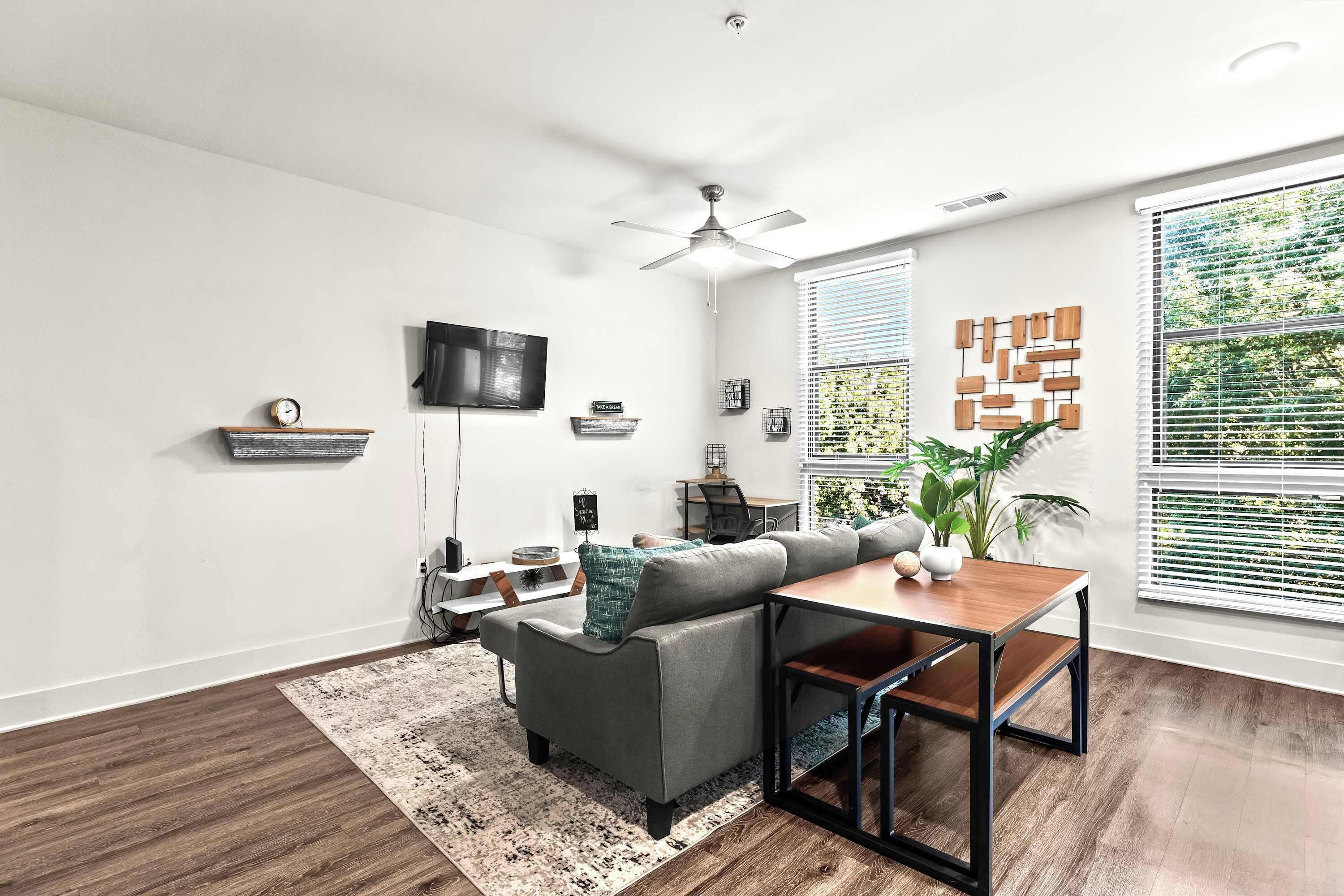 Un salon moderne avec un canapé gris, une table basse en bois et un ventilateur de plafond.