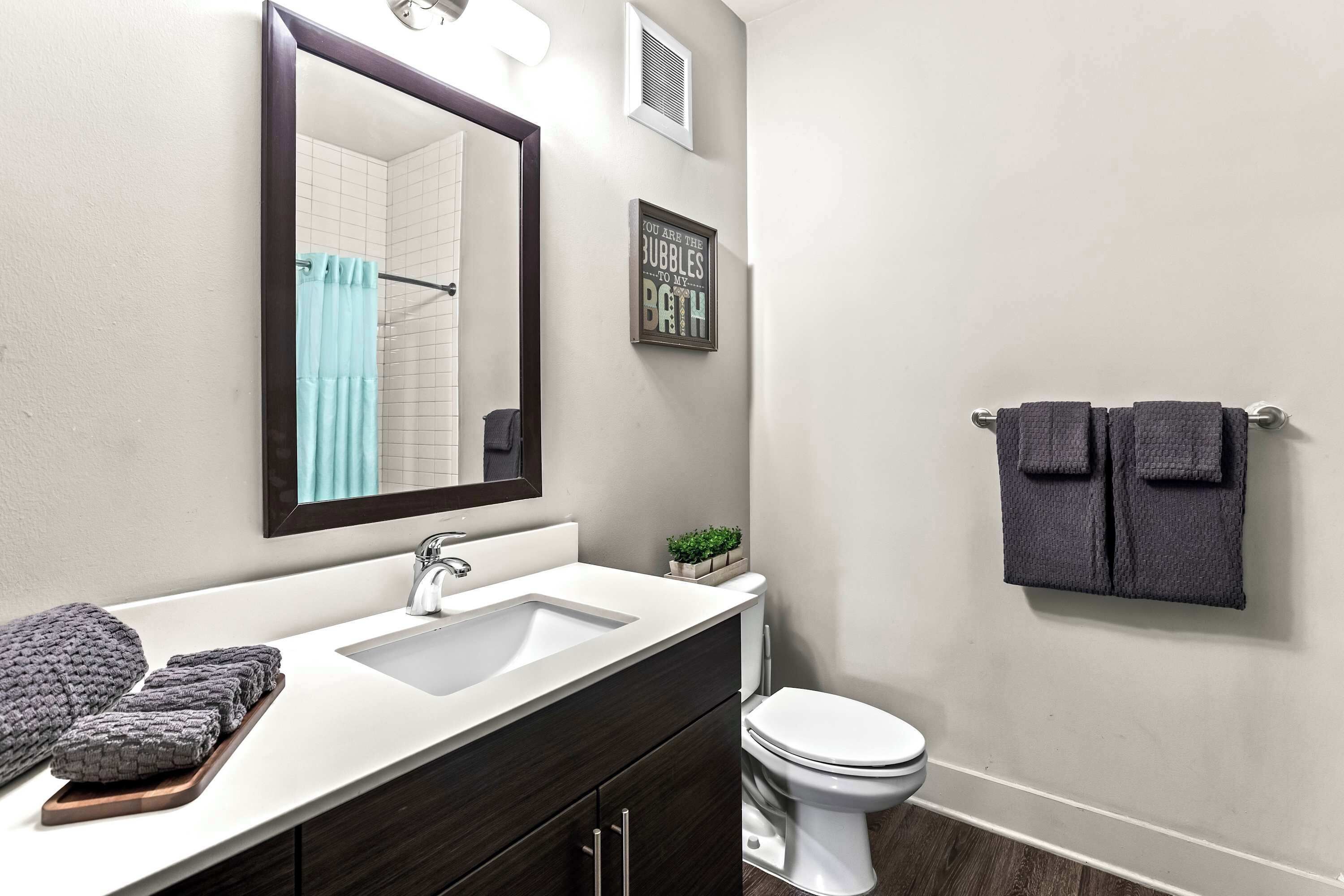 Une salle de bain moderne avec un lavabo blanc, un meuble-lavabo en bois foncé, des toilettes blanches et un porte-serviettes avec deux serviettes.