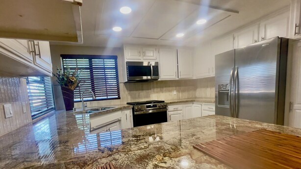 A modern kitchen with white cabinets, a stainless steel refrigerator, and a granite countertop.