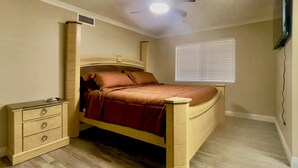 A bedroom with a wooden bed, a nightstand, a dresser, a ceiling fan, and a window with blinds.