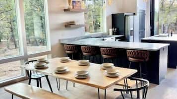 A modern kitchen with a large island, a dining area with a bench, and large windows offering a view of the outdoors.