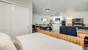 Quarto com cama, cabeceira de madeira e vista para a área da cozinha adjacente.