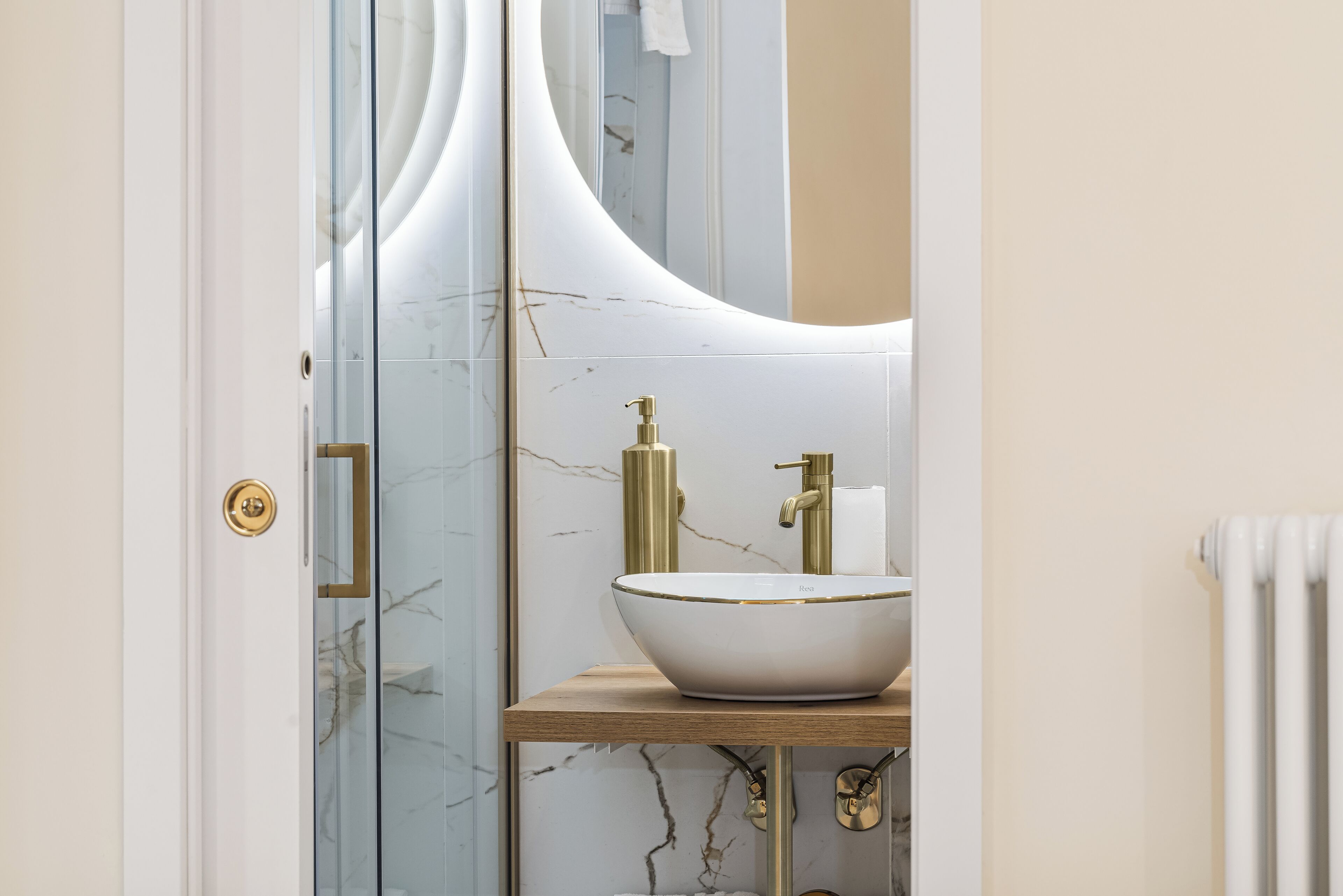 A bathroom with a white marble sink, gold fixtures, and a curved mirror.