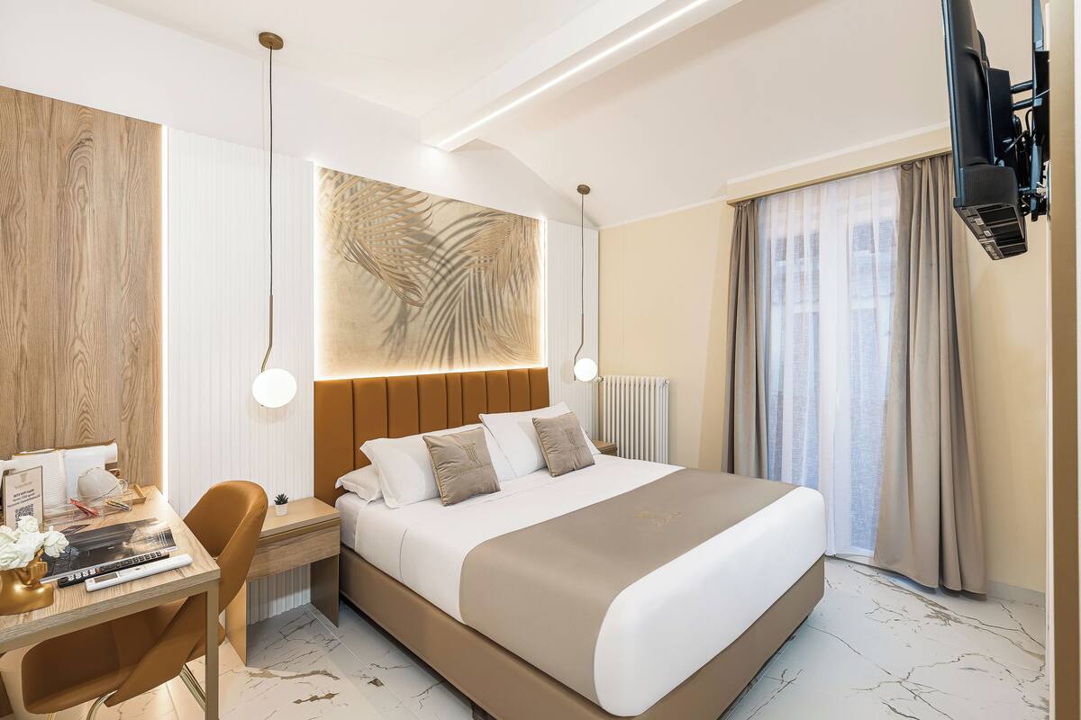 Ein modernes Hotelzimmer mit einem großen Bett, einem Schreibtisch mit Stuhl, einem Fernseher und einem großen Fenster mit Vorhängen.