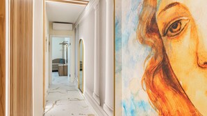 A hallway with white walls, marble flooring, and a large painting of a woman's face. - La Casa delle Dee – Self Check-in (Bologna)