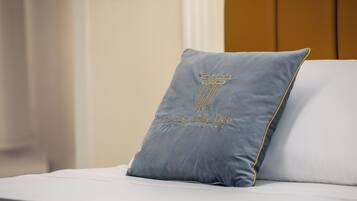 Un lit avec un oreiller gris orné d’un motif en forme de colonne et sur lequel on peut lire l’inscription « La Casa delle Dee » sur un couvre-lit blanc.