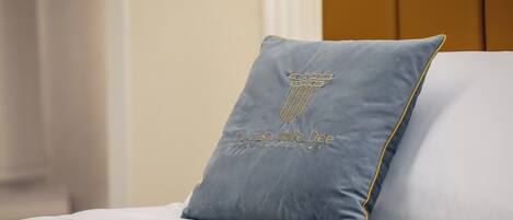 A bed with a grey pillow featuring a column design and the text "La Casa delle Dee" on a white bedspread.