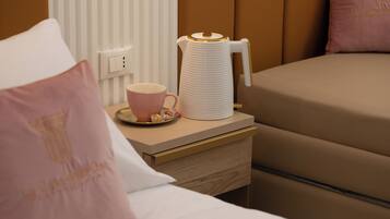 A neatly made bed with a pink pillow, a bedside table with a white coffee maker, and a pink cup.