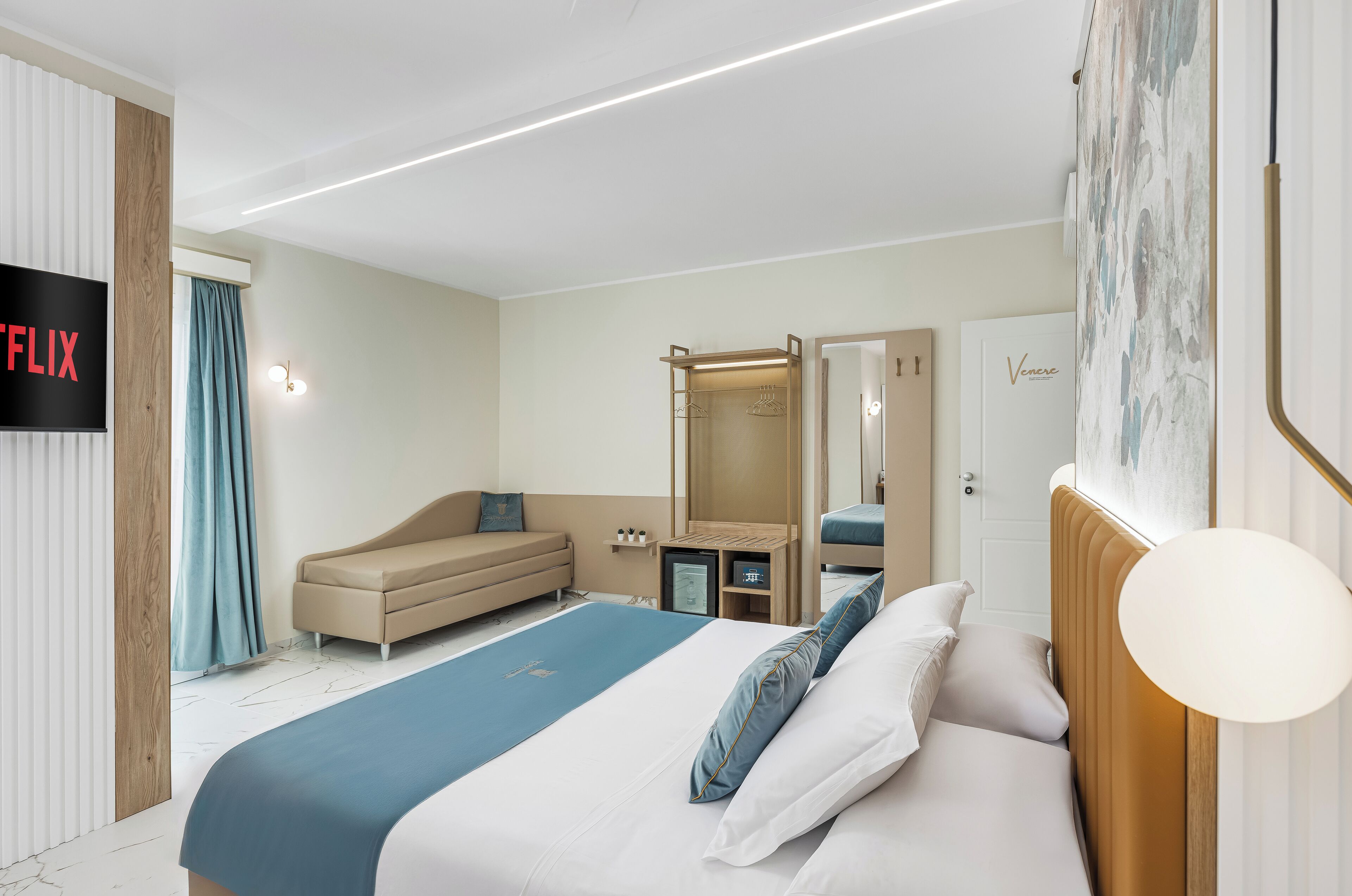 A modern hotel room with a bed, a sofa, a wardrobe, a TV, and a mirror.