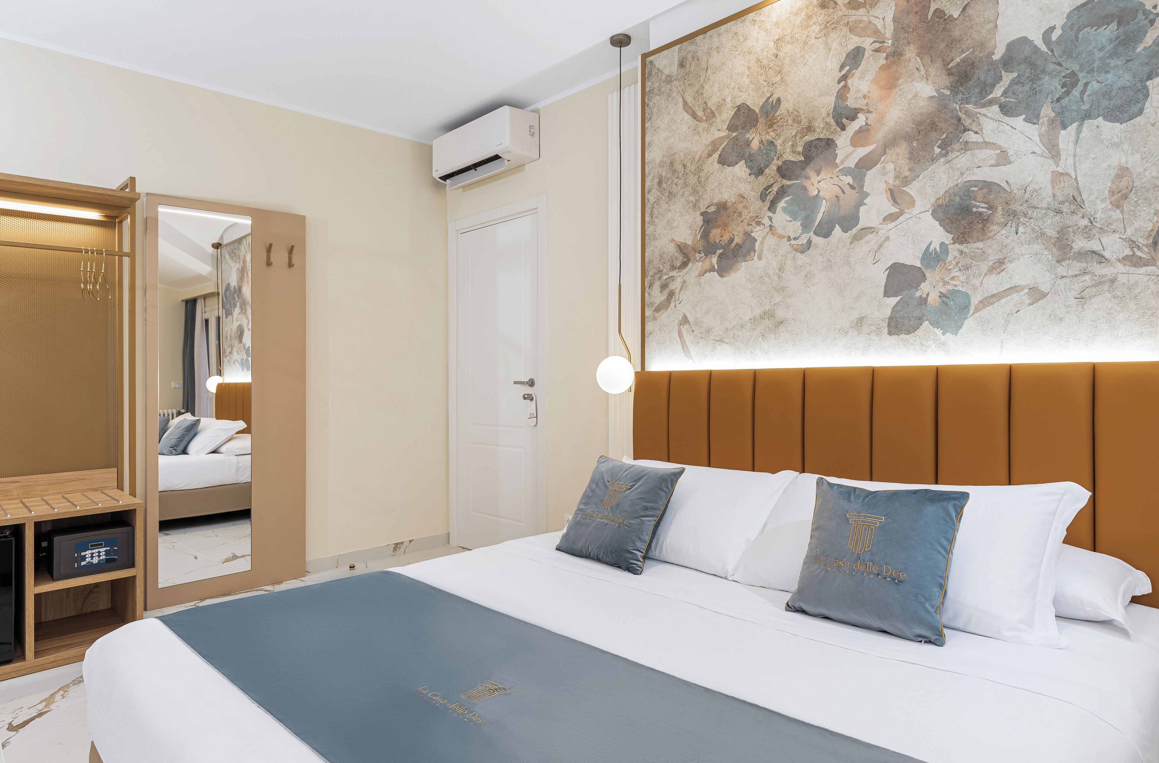 Quarto de hotel com cama, guarda-roupa, espelho e ar condicionado fixado na parede.