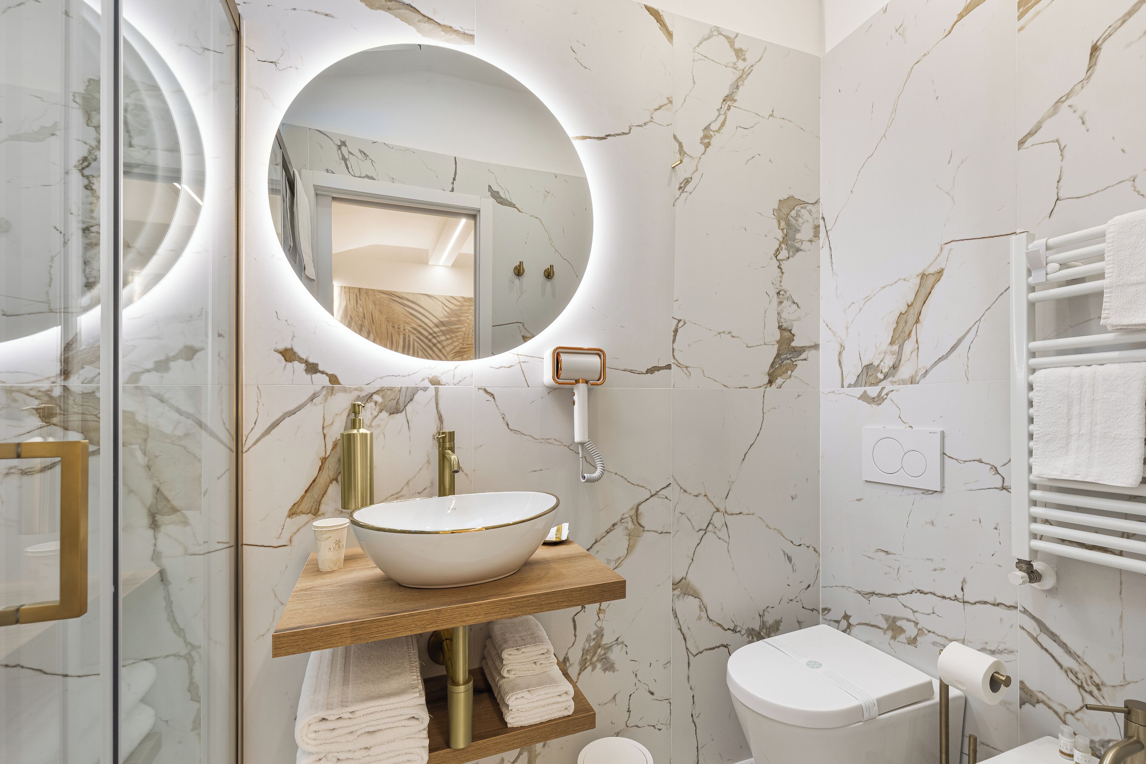 Ein modernes Badezimmer mit Marmor-Spritzschutz, einem runden Spiegel, einem Aufsatzwaschbecken und einer Toilette.