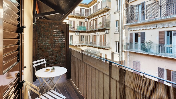 A balcony with a table and chairs, a wooden door, and a view of neighboring buildings. - La Casa delle Dee – Self Check-in (Bologna)