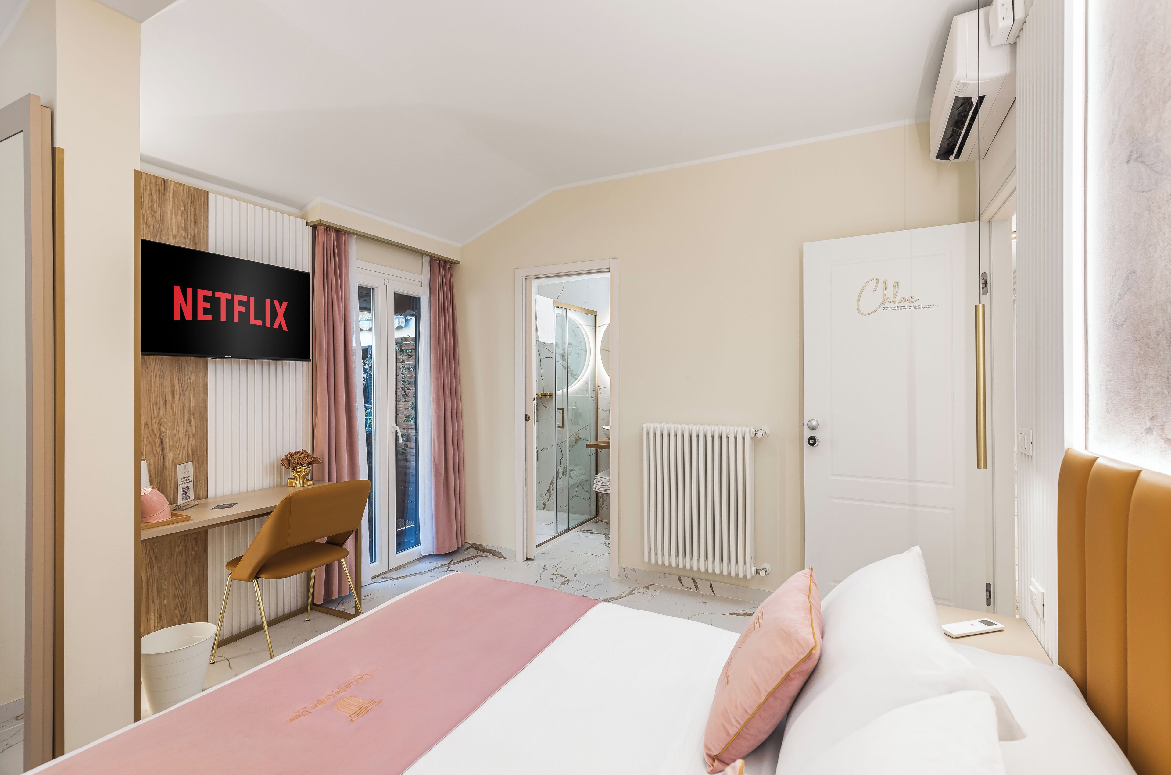 A modern hotel room with a bed, a desk, a TV displaying 'NETFLIX', and a door labeled 'Chloe'.