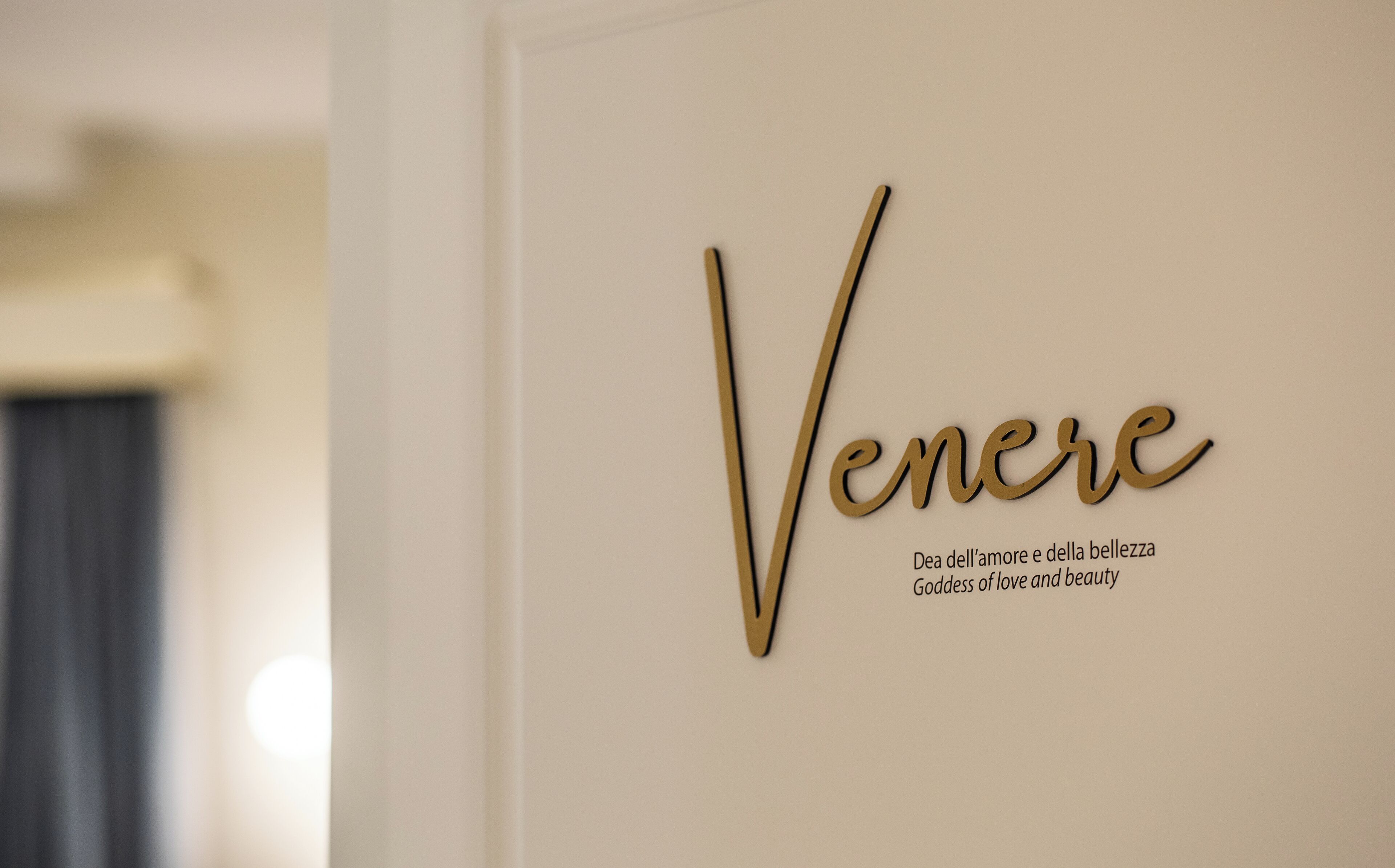 Een muur met de naam 'Venere' en de tekst 'Dea dell'amore e della bellezza Godin van liefde en schoonheid' in gouden letters.