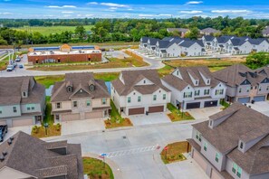 A residential area with detached houses, a commercial building, and a clear sky. - The Tigers Pathway House near LSU Stadium - BC1034 (Baton Rouge)