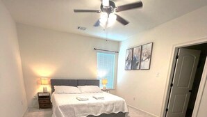 A bedroom with a bed, a ceiling fan, a nightstand, a lamp, and a window with blinds. - The Tigers Pathway House near LSU Stadium - BC1034 (Baton Rouge)