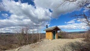 Pieni puinen mökki, jossa on vihreä ovi, ja sen ympärillä on kivituhkapolku ja niukasti kasvillisuutta.