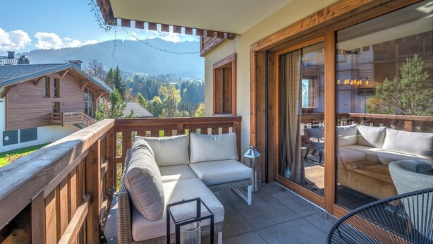 Een balkon met een houten terras, een bank, een stoel en een tafel.