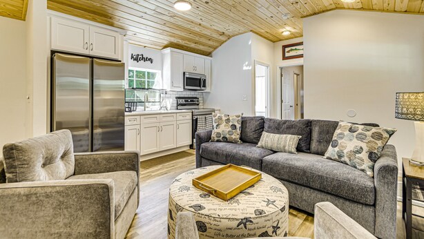 Ein modernes Wohnzimmer mit einem grauen Sofa, einem Holztisch und einer Küche im Hintergrund.
