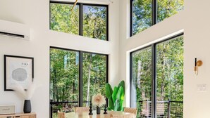 Ein moderner Essbereich mit einem runden Tisch, Korbstühlen und einem großen Fenster mit Blick auf Grünflächen.