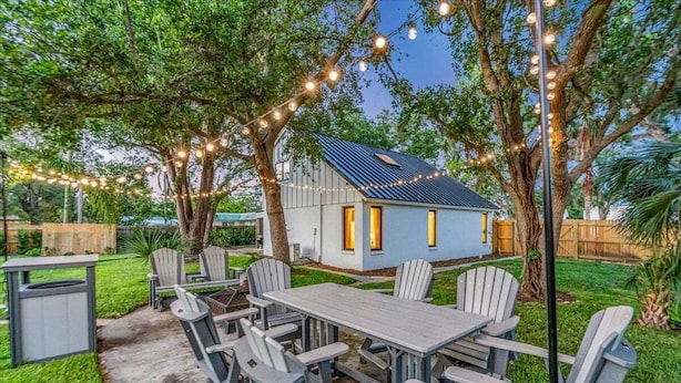 Une terrasse avec une table et des chaises, entourée d’arbres et illuminée de guirlandes lumineuses.