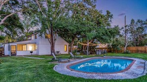 Une maison avec une piscine, entourée d’une pelouse bien entretenue et d’arbres.