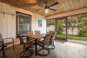 Une terrasse couverte avec une table et des chaises, un ventilateur de plafond et une vue sur l’extérieur.