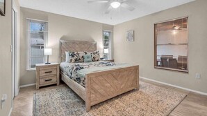 Une chambre à coucher avec un lit en bois, une table de chevet, un ventilateur de plafond et une fenêtre avec des stores.
