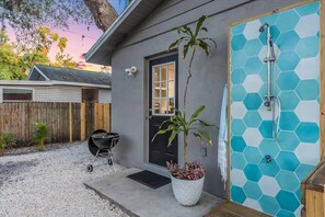Une maison à l’extérieur grise, avec une porte noire et une cabine de douche à motifs hexagonaux.