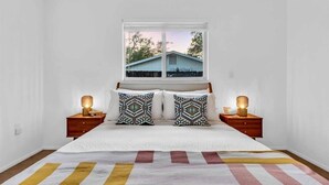 A bedroom with a bed, two bedside tables, two lamps, a window with a view of a house, and a striped rug. - CandyPop Retro Retreat | Ms Pac-Man Game + Patio (Sarasota)