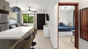 A modern kitchen with a dining area, a bedroom with a bed and a view, and a bathroom with a shower and toilet. - Lovely modern 2 bedroom gated condo, walk to the beach and town center (Playas del Coco)