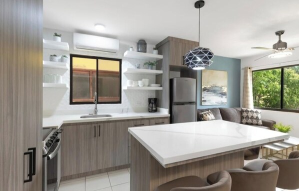 Une cuisine moderne dotée d’un grand îlot central, d’un vaste espace de préparation, d’appareils électroménagers de taille standard et de nombreux rangements.