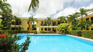 A pool surrounded by lush greenery and a yellow building with multiple balconies. - Lovely modern 2 bedroom gated condo, walk to the beach and town center (Playas del Coco)