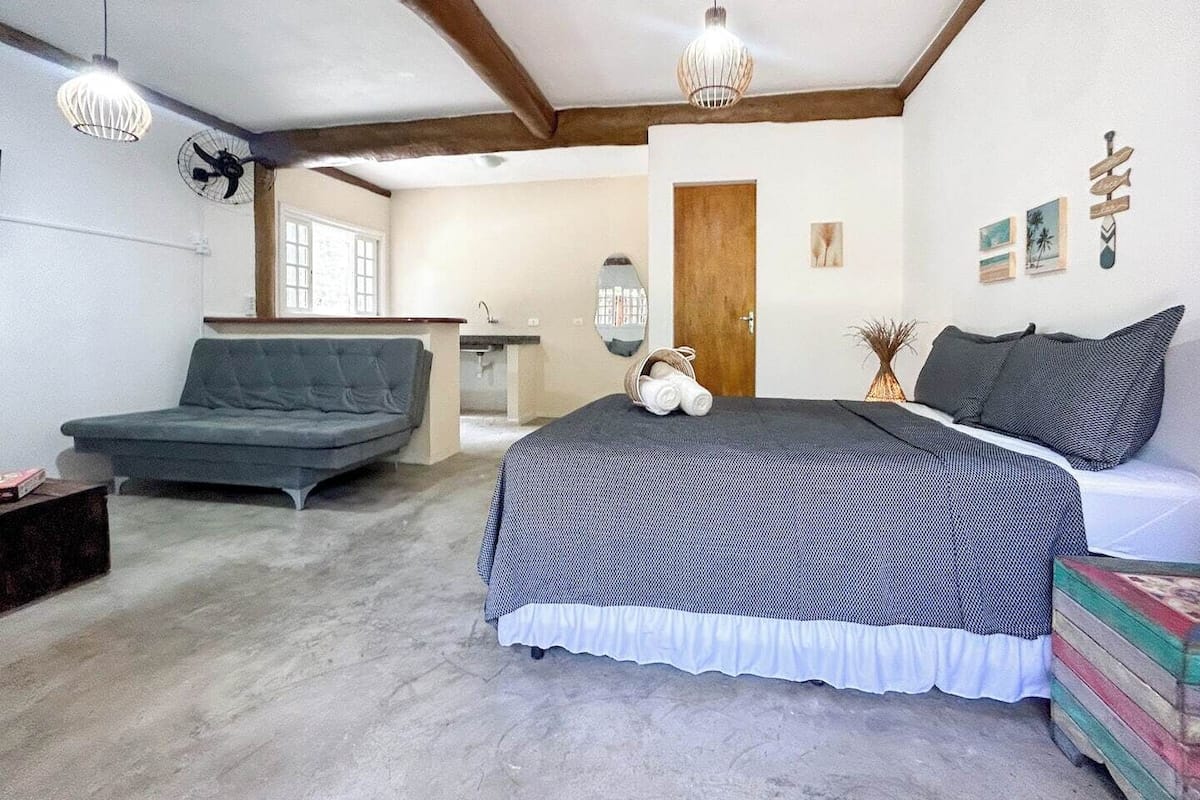A bedroom with a bed, a sofa, a small table, and a fan.