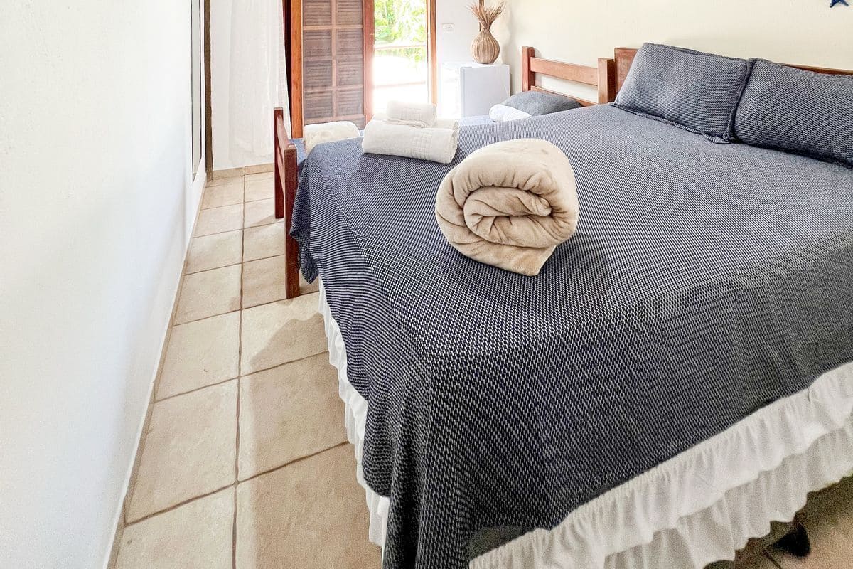 A bedroom with a wooden ceiling, a bed with a striped bedspread, a ceiling fan, and a wall-mounted TV.