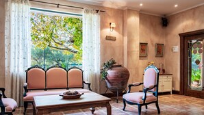 A room with a large window, a wooden table, striped chairs, a potted plant, and a wall-mounted light fixture.