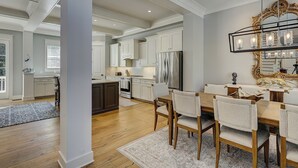 Una cocina amplia con muebles blancos, un refrigerador de acero inoxidable y un comedor con candelabro.