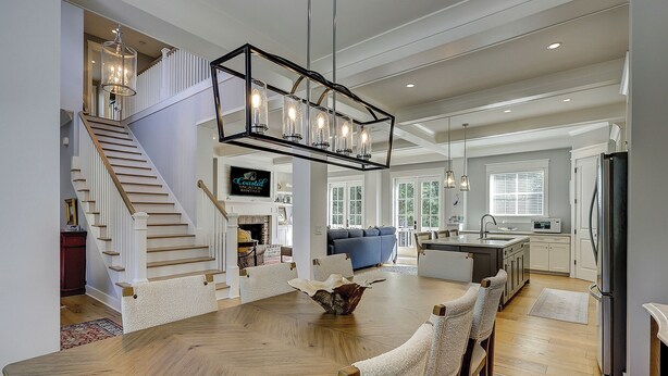 Amplia sala de estar con mesa de comedor de madera, una escalera y zona de cocina.