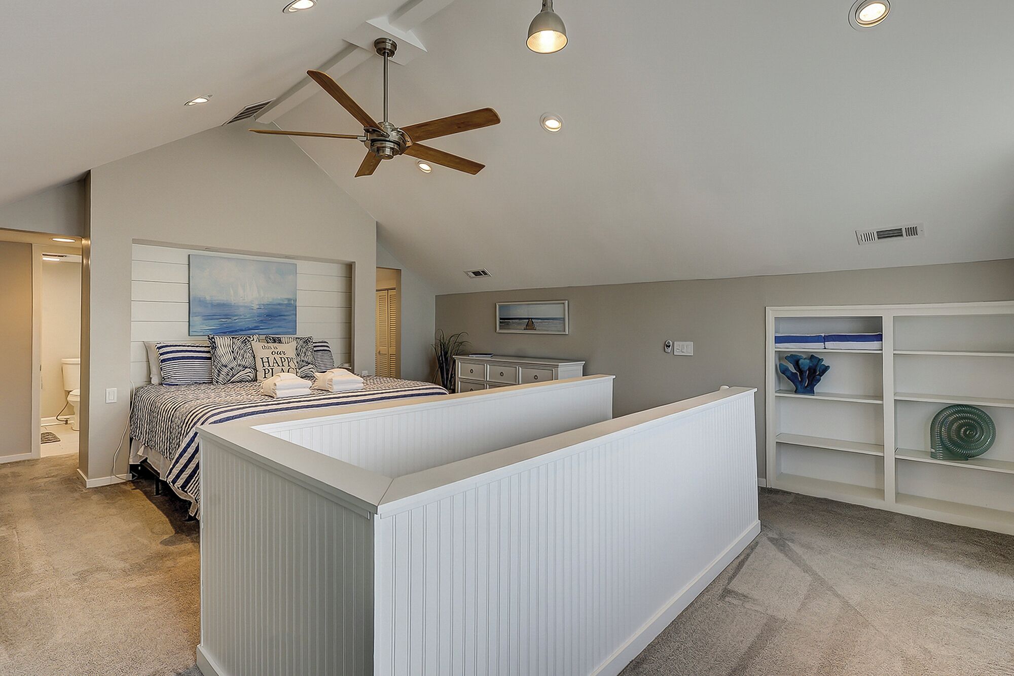Un dormitorio con cama, ventilador de techo, iluminación empotrada, estantería y vistas al exterior.