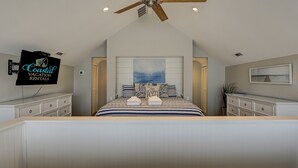 Quarto com cama, ventoinha no teto, televisão e quadro na parede.