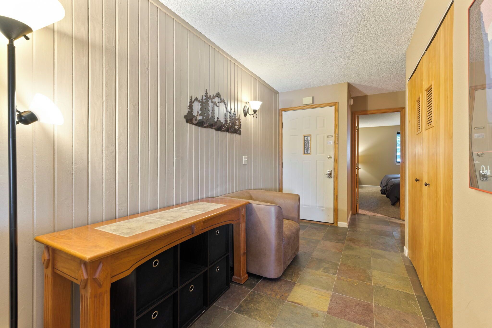 A hallway with a wooden bench, a wall-mounted light fixture, and a door leading to another room.