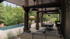 Ein überdachter Patio-Bereich mit Gartenmöbeln, einem Pool und üppiger Bepflanzung im Hintergrund.