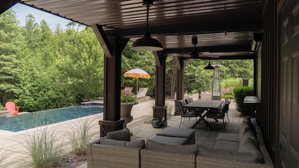 A covered patio area with outdoor furniture, a pool, and lush greenery in the background.
