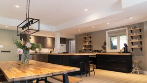 Eine moderne Küche mit einem Holztisch, schwarzen Barhocker und einer hängenden Leuchte.