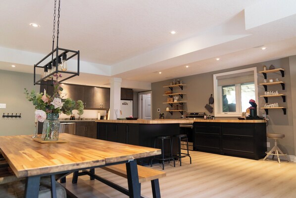 A modern kitchen with a wooden dining table, black bar stools, and a hanging light fixture.