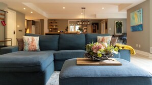 A modern living room with a sectional sofa, a coffee table with a floral arrangement, and a dining area in the background.
